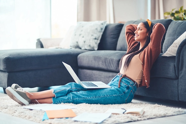a student sitting on the floor with her laptop taking a break from homework and looking up